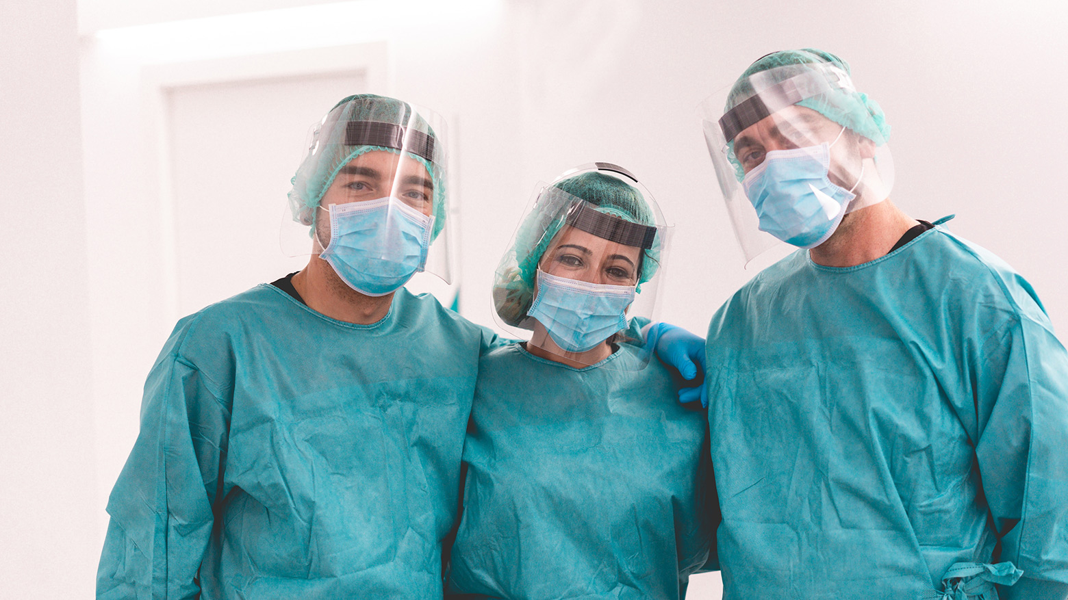 Three health-care workers standing side-by-side in full personal protective equipment (masks, face shields and gowns) 