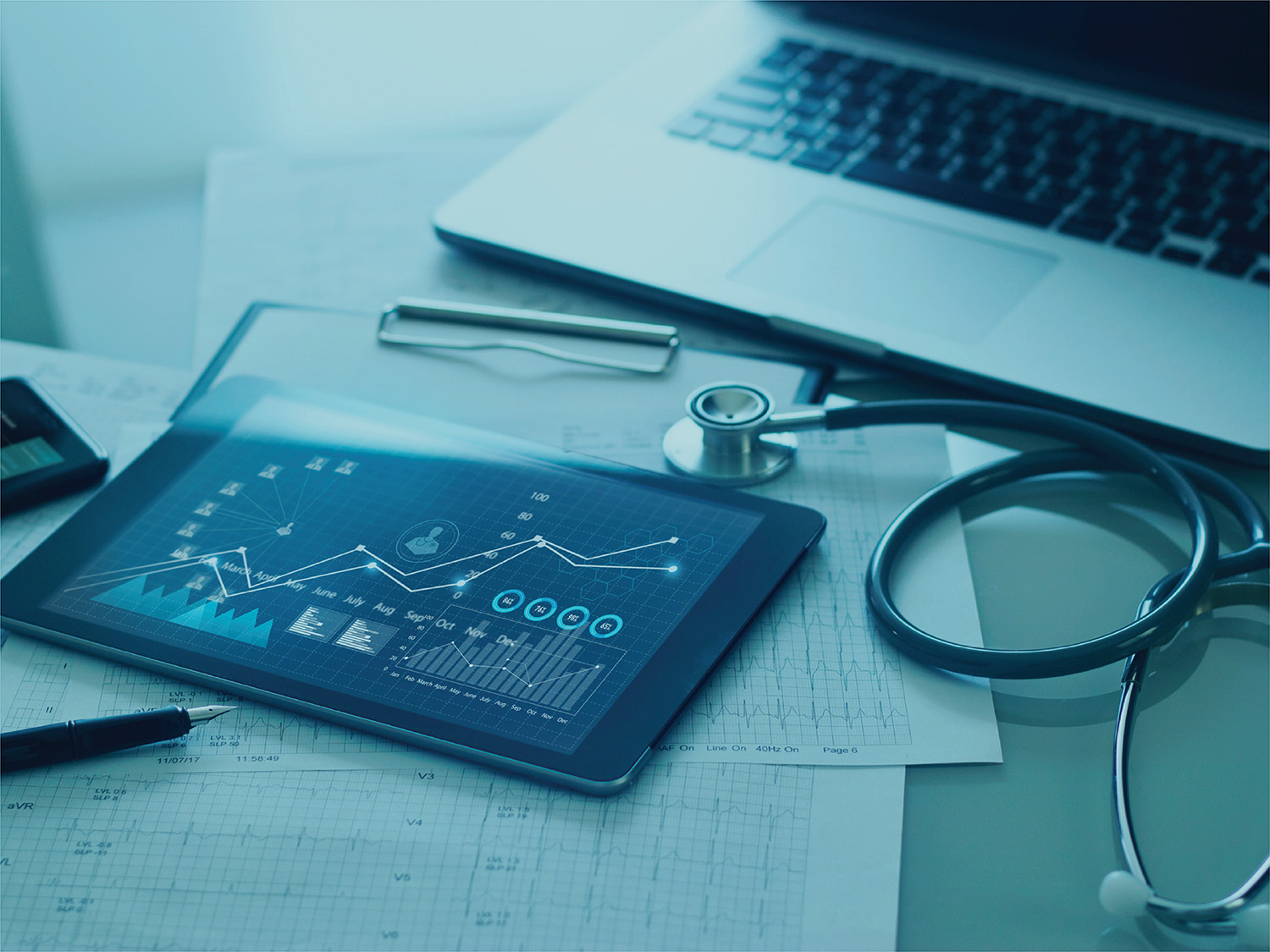 A stethoscope, tablet, papers and laptop on a desk