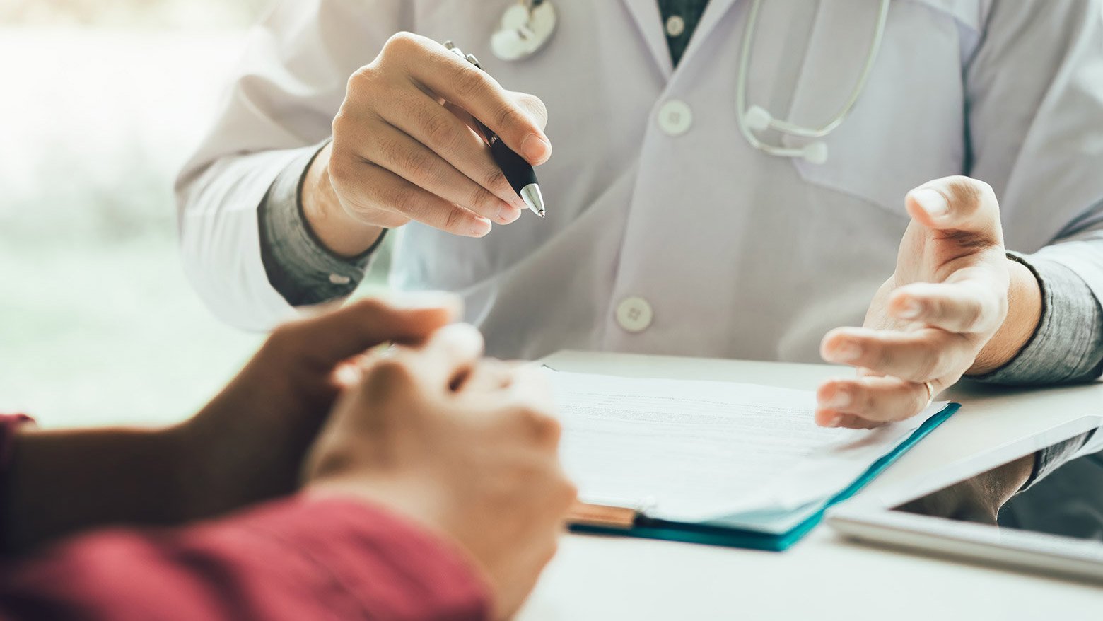 Doctor sits at a desk with a patient to discuss paperwork