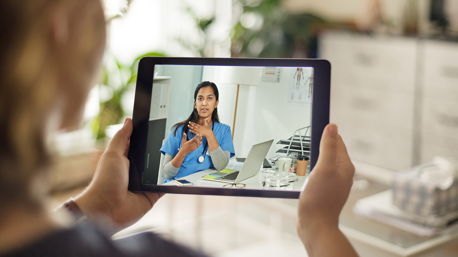 Woman holds up a tablet to have a video call with her doctor