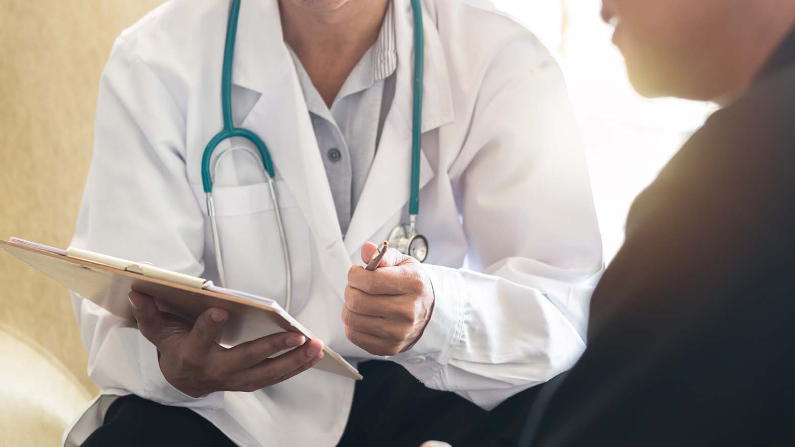 A doctor holds out a clipboard and pen to a patient