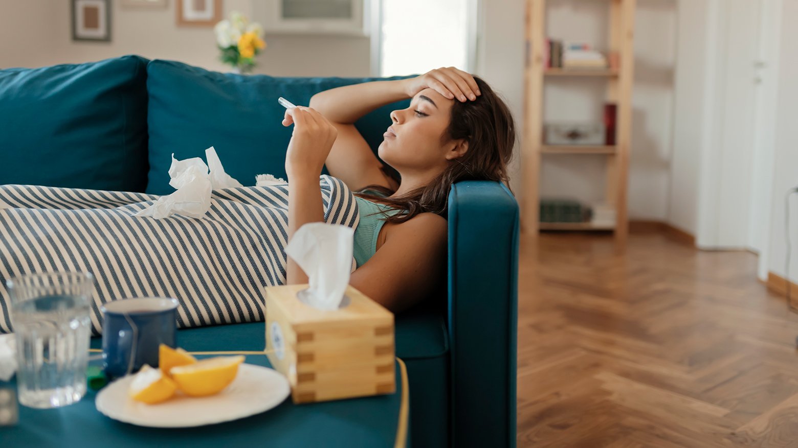 A woman checks her temperature as she lays on a sofa