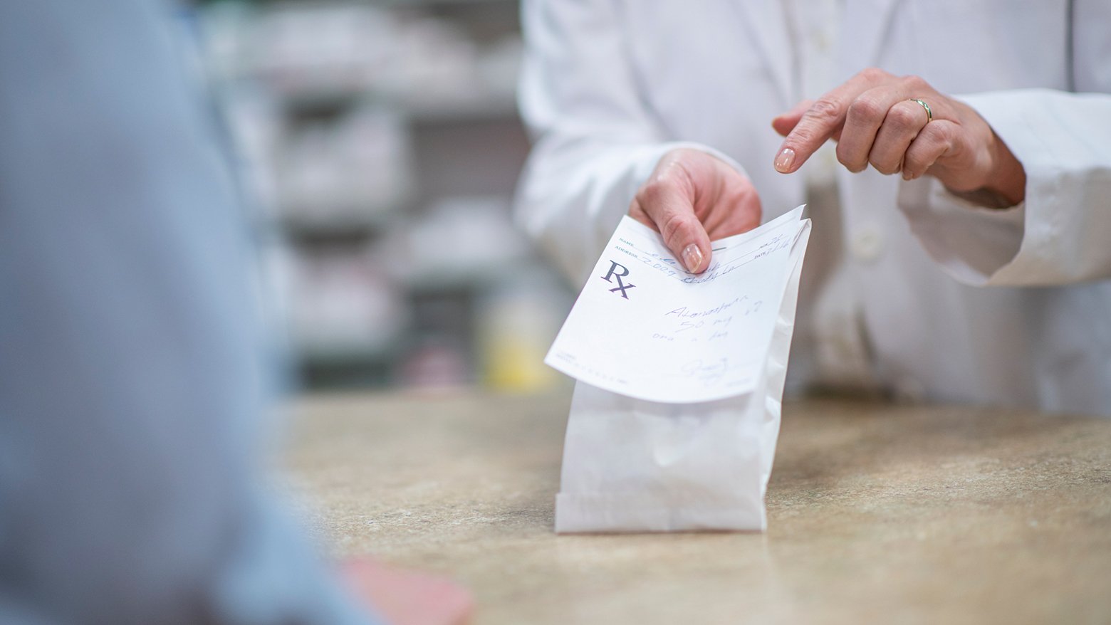 A pharmacist hands a prescription to a customer