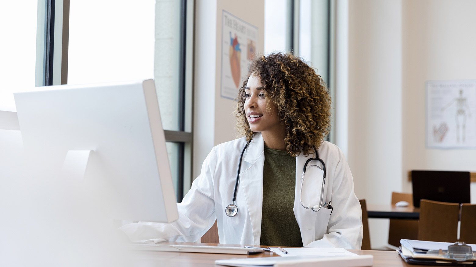 A female doctor sits at a desk and looks at a computer screen