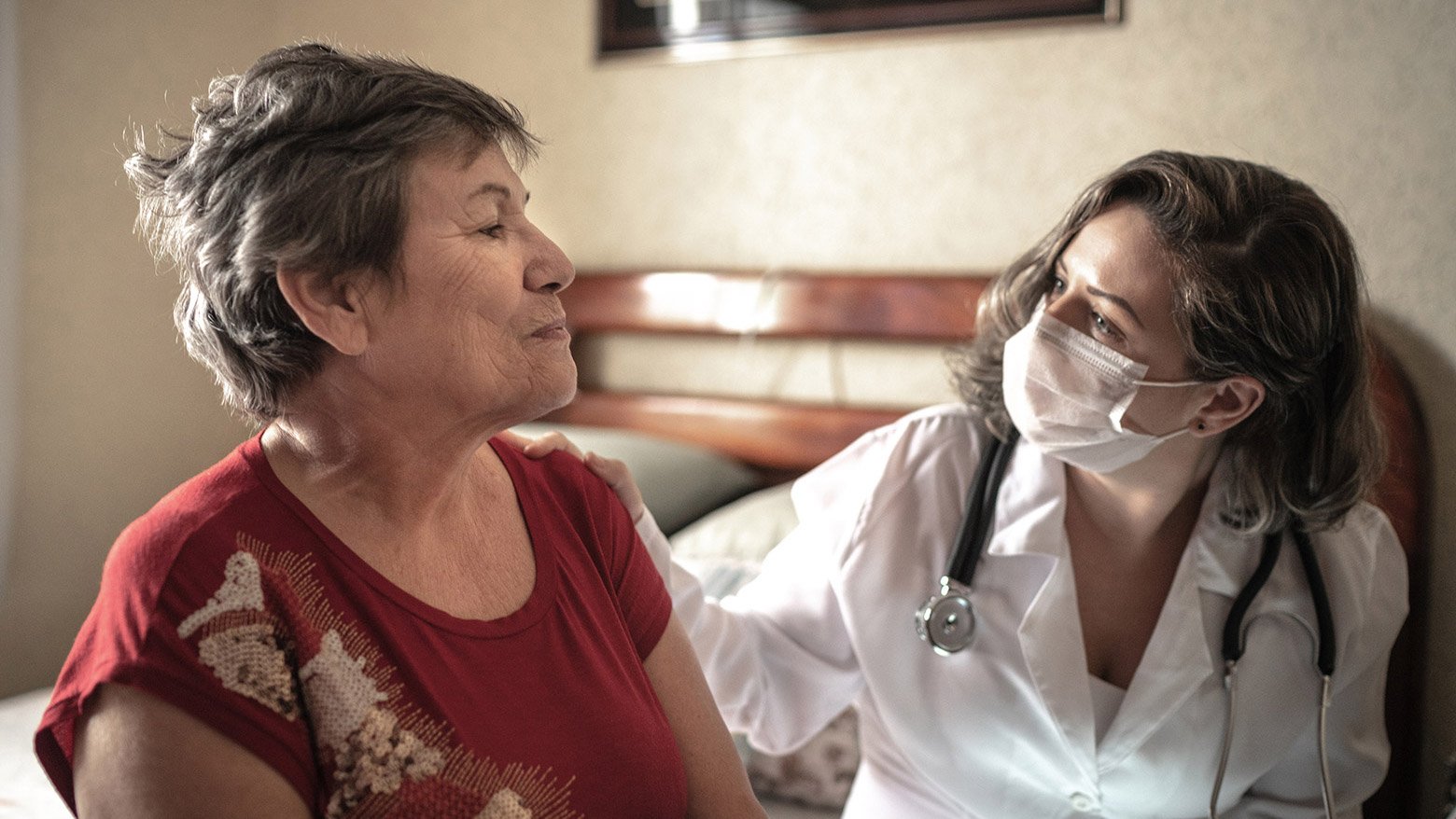A female doctor wears a medical mask while speaking to a female patient that sits beside her