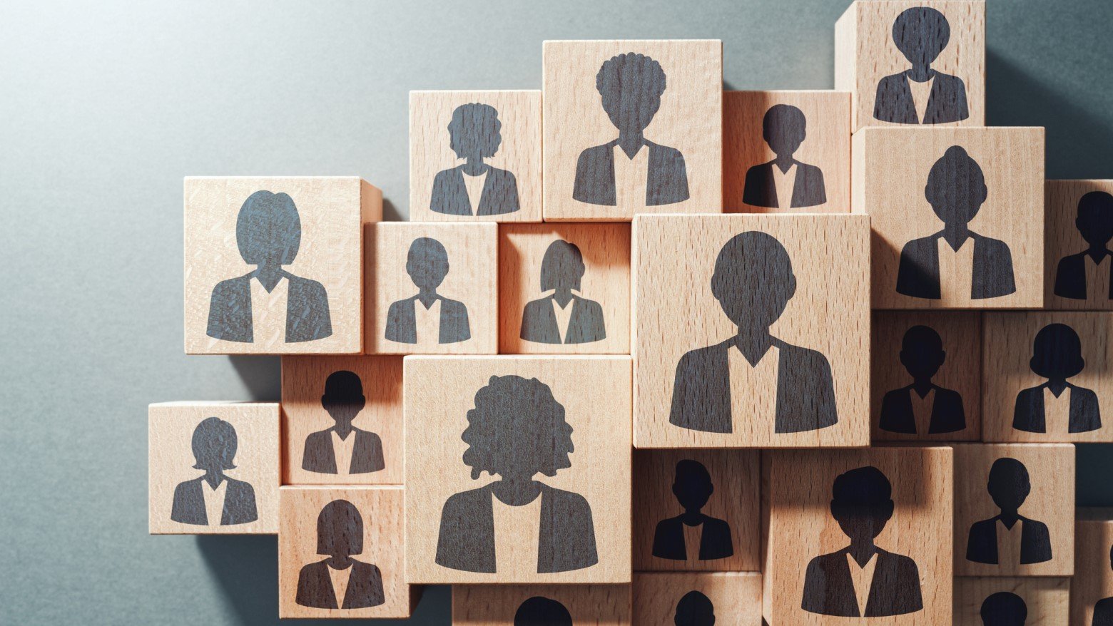 A pile of wooden blocks with printed silhouettes of diverse individuals, symbolizing teamwork and community representation.