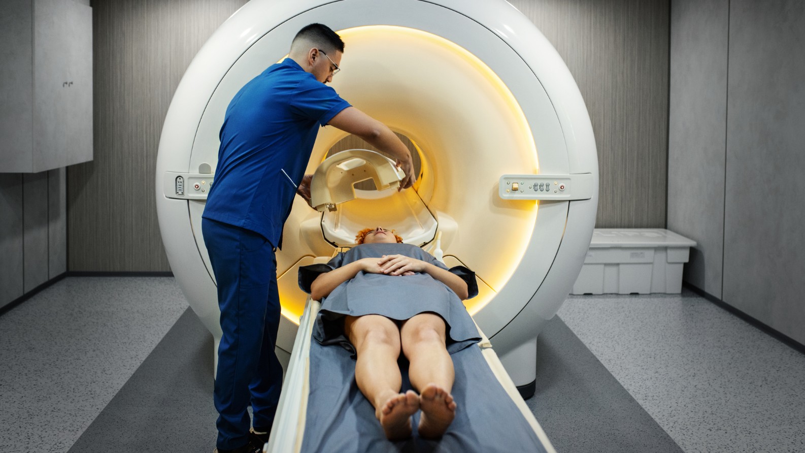 A technician stands next to the MRI machine and prepares the patient for the examination.