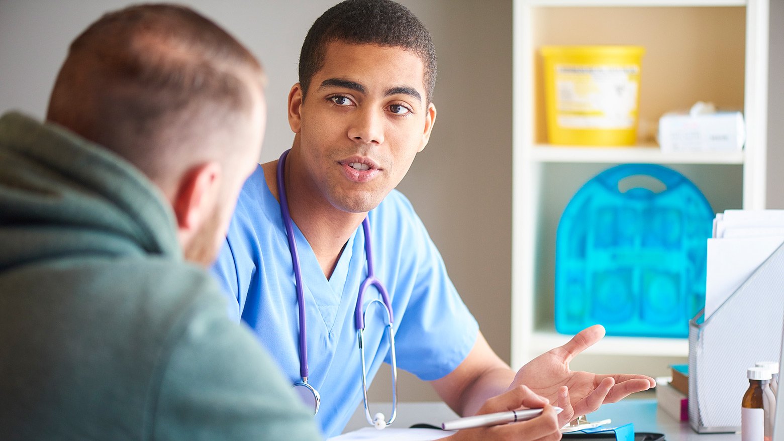 A male doctor in scrubs speaking to a patient. 