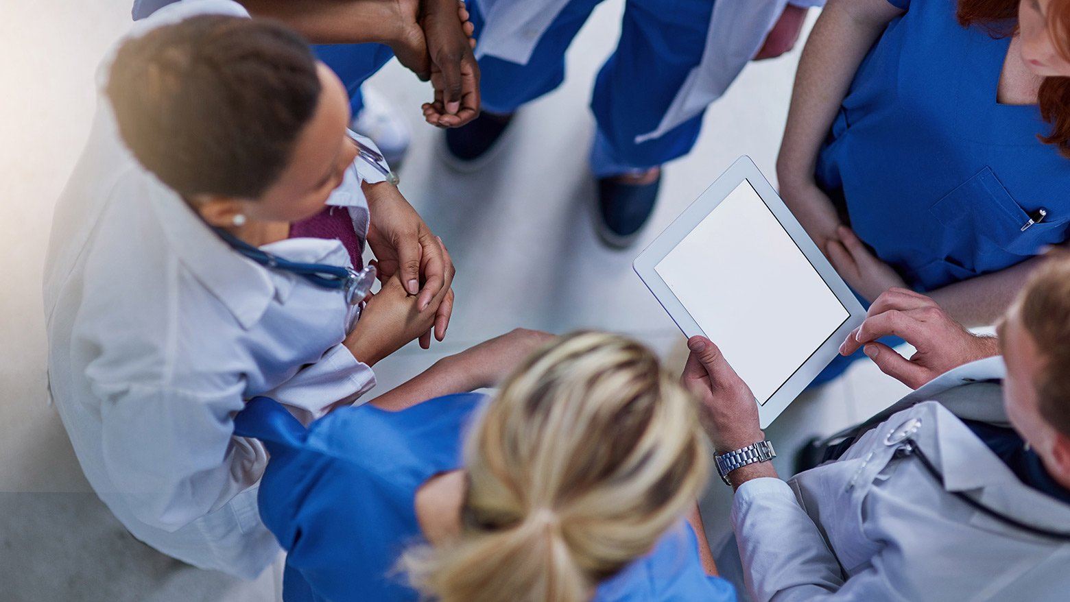 A group of doctors huddle together to review a document on a tablet