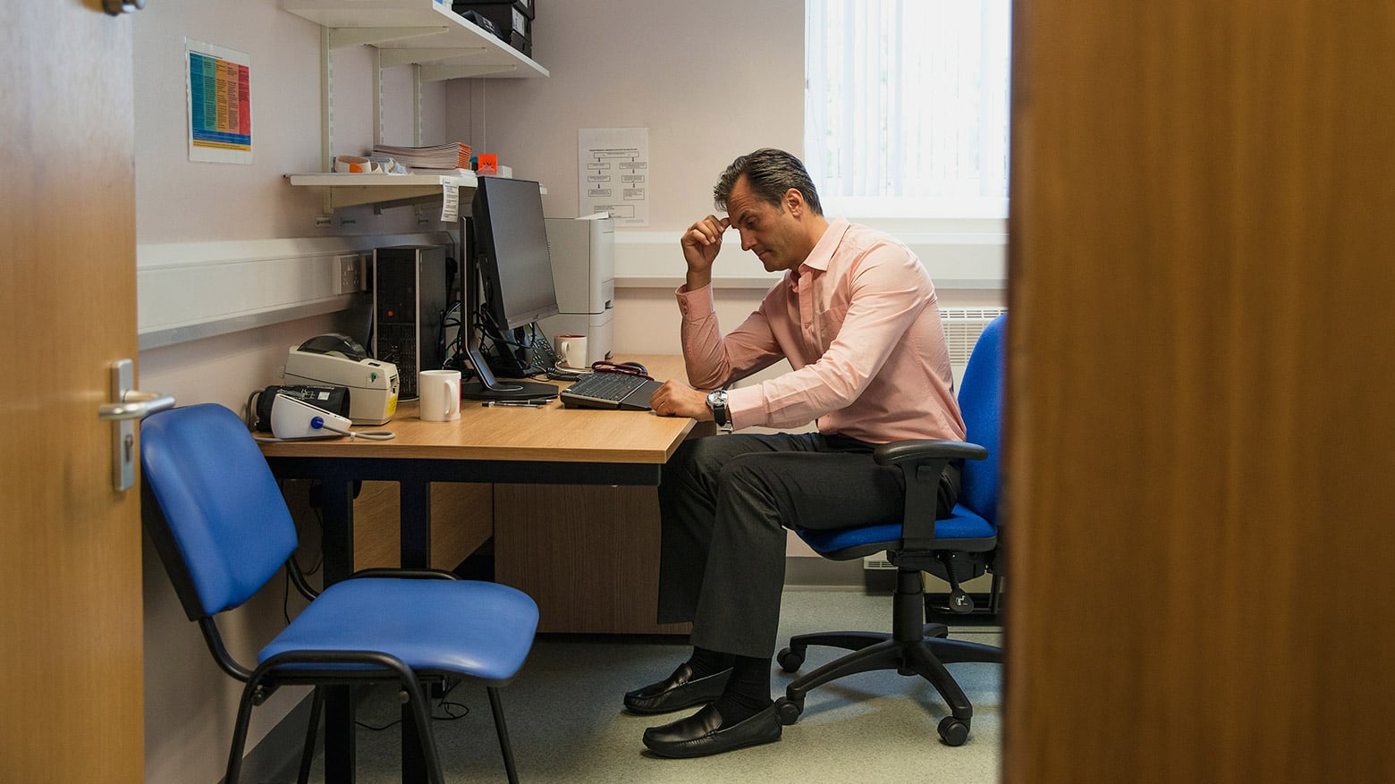 A man sits at a desk while holding his hand to his head