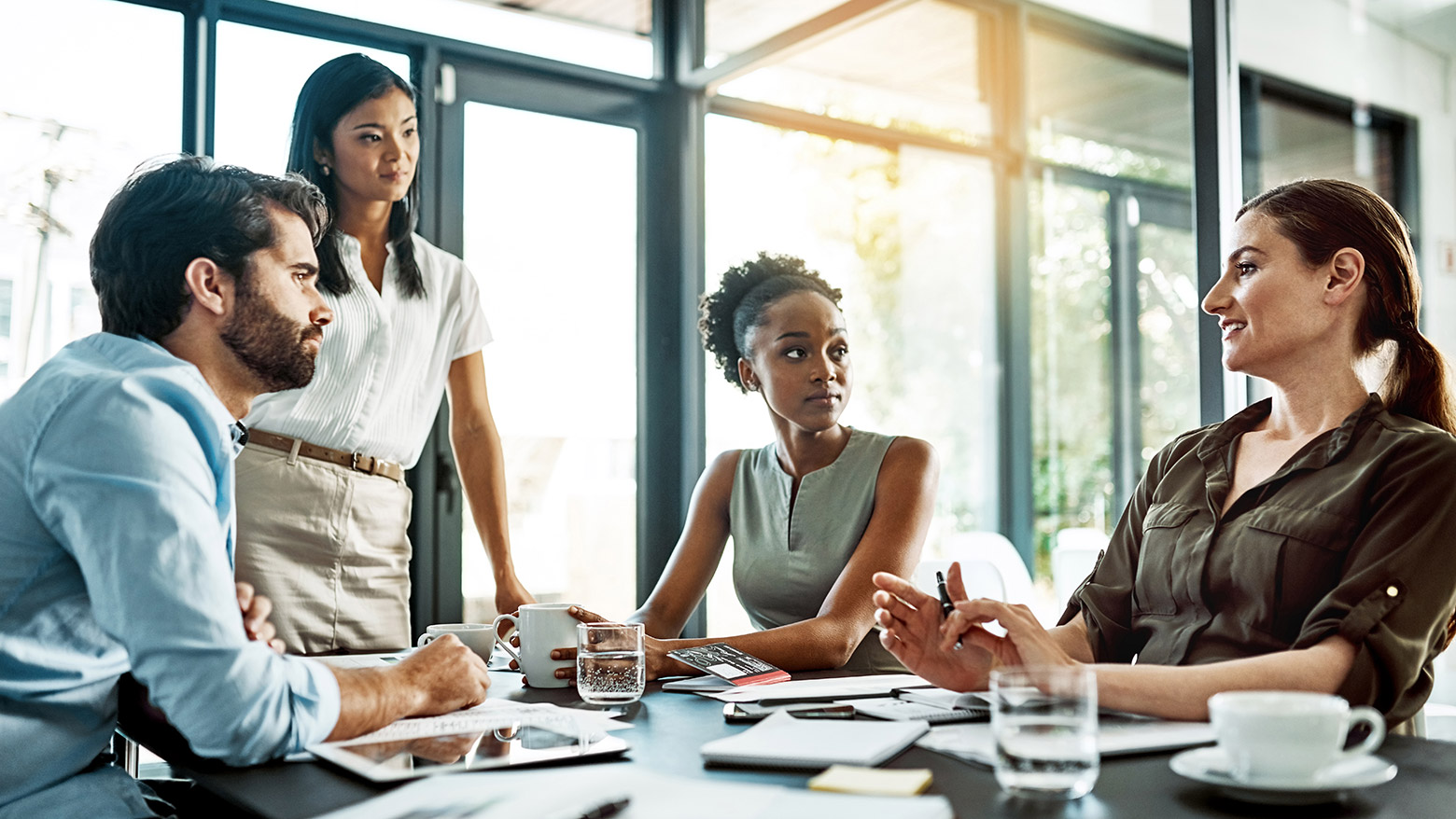 A man and three women at a table listening to a woman speak. 