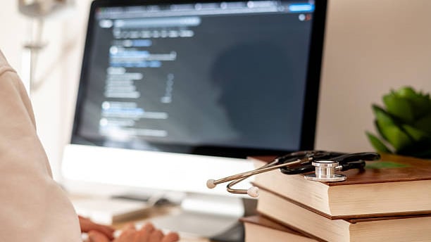 Doctor is programming an ai chatbot for healthcare, symbolizing the future of medical learning and telemedicine, with a stethoscope resting on medical books in the foreground