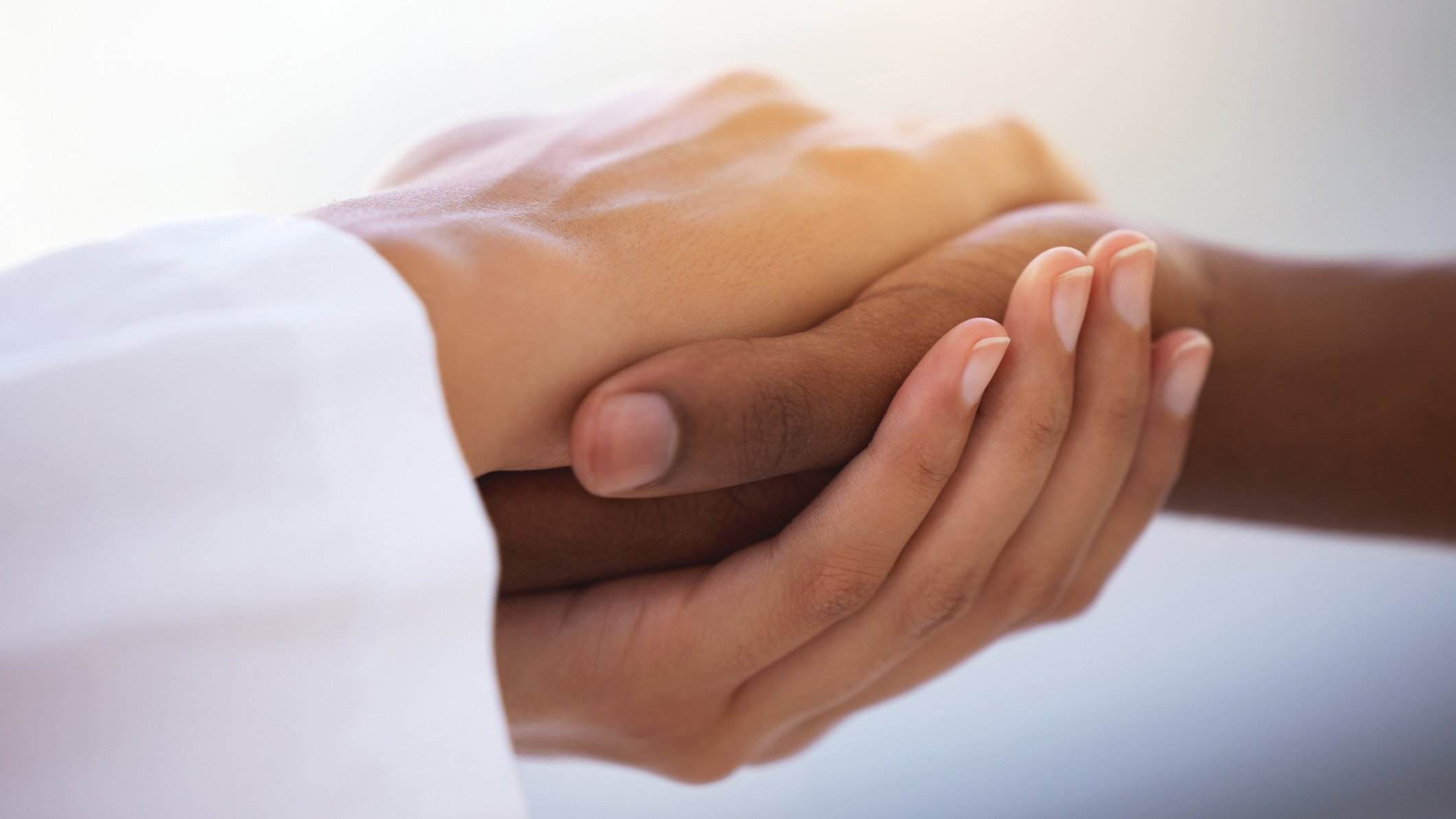 Two hands of different skin tones clasped together, symbolizing unity and support in a soft, well-lit background.