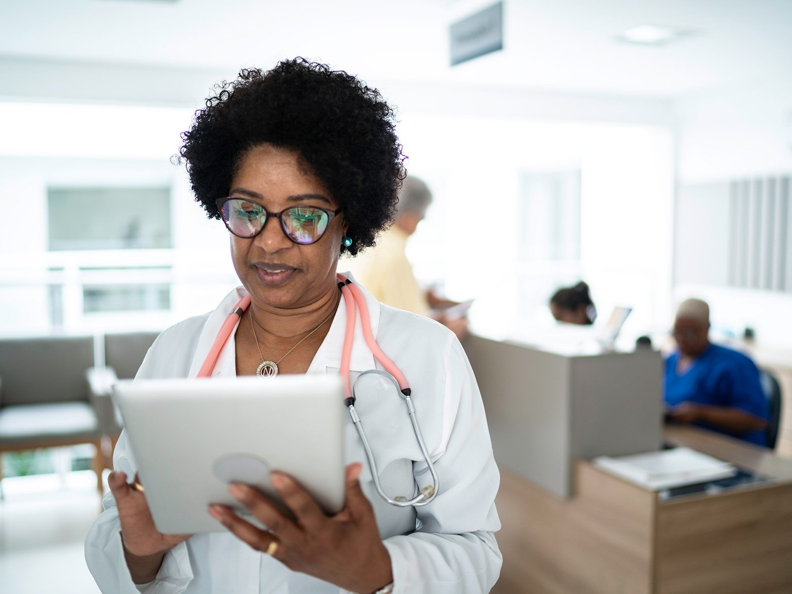 Female physician looks at her iPad in front of a doctor's desk.