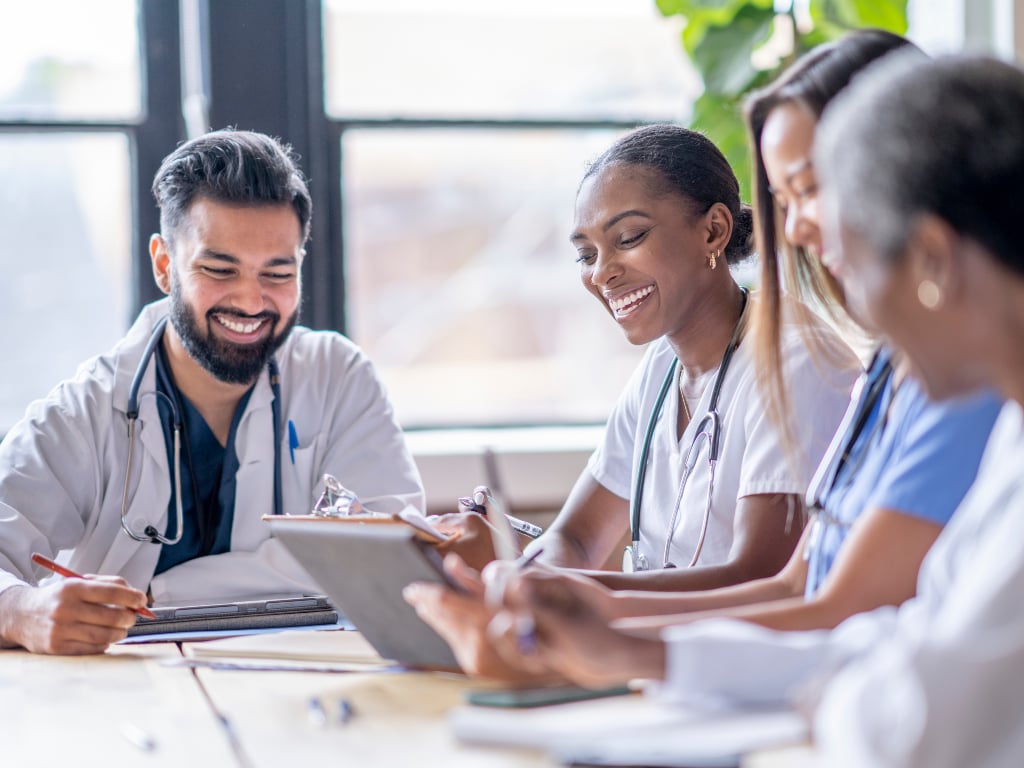 A small group of four medical professionals sit around a boardroom table.