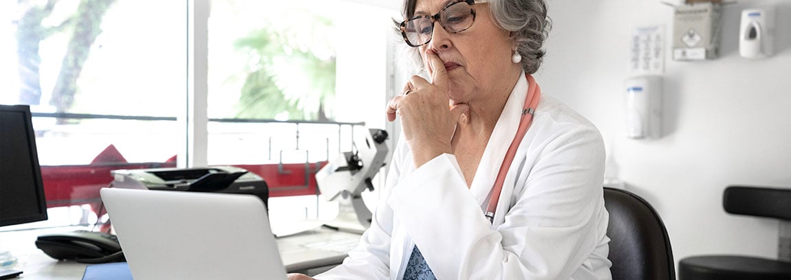 An older female doctors looks pensive while using her laptop
