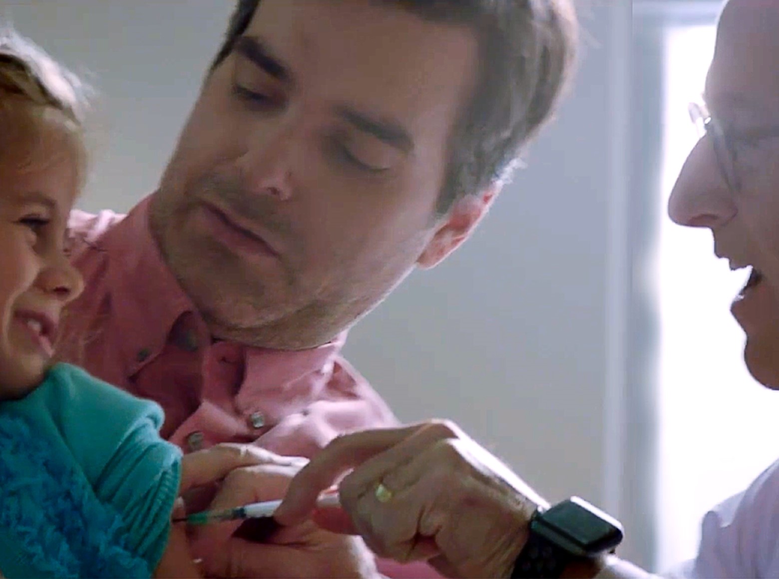 Father holding a child while physician  ooks on