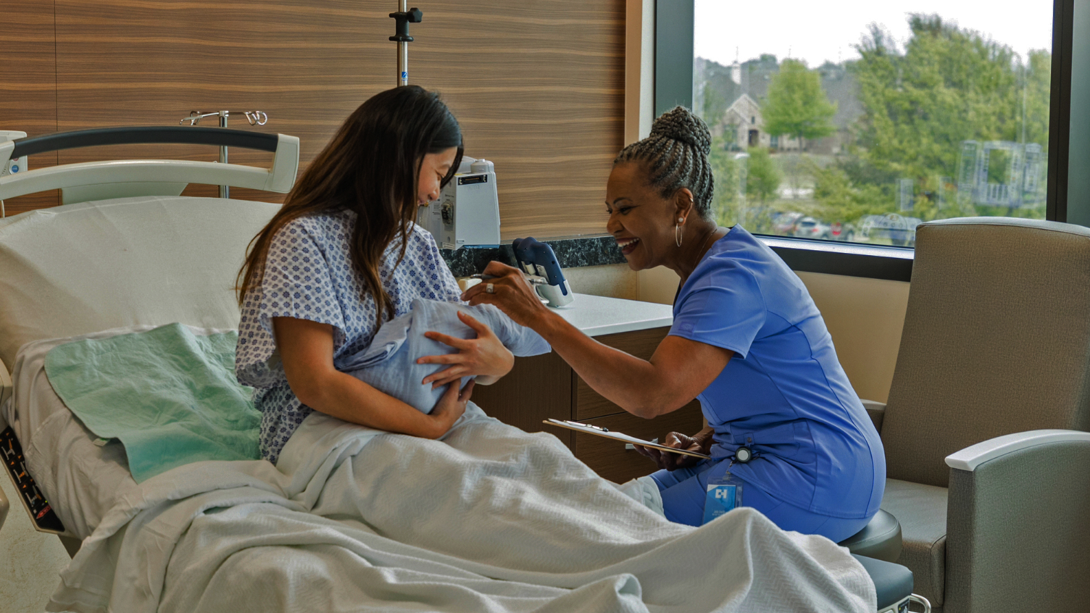 A physician sitting with a mother and baby at their hospital bed
