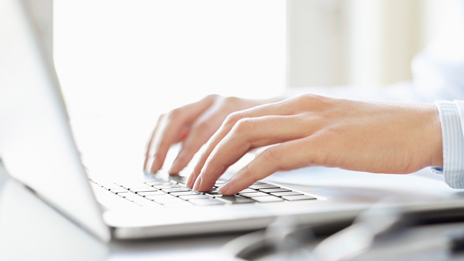 Hands are pictured typing on a laptop computer.
