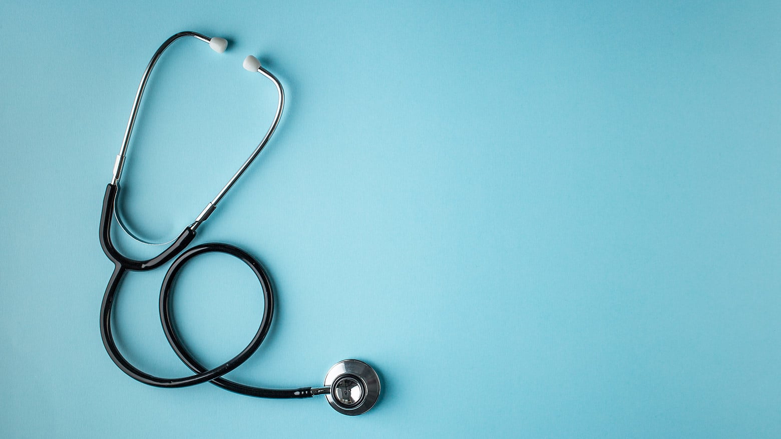 A stethoscope placed on a light blue background. The stethoscope has black tubing and silver chest pieces.