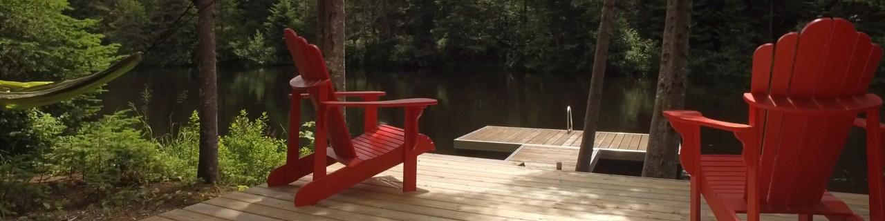 Two Muskoka chairs site on a deck by a lake