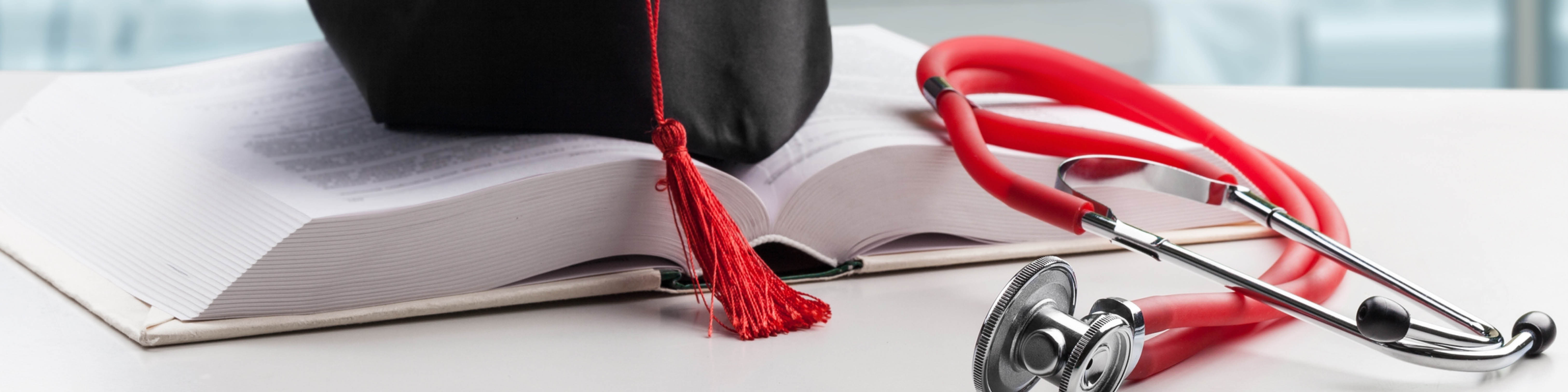 A graduation cap sits atop an open book, behind a red stethoscope.
