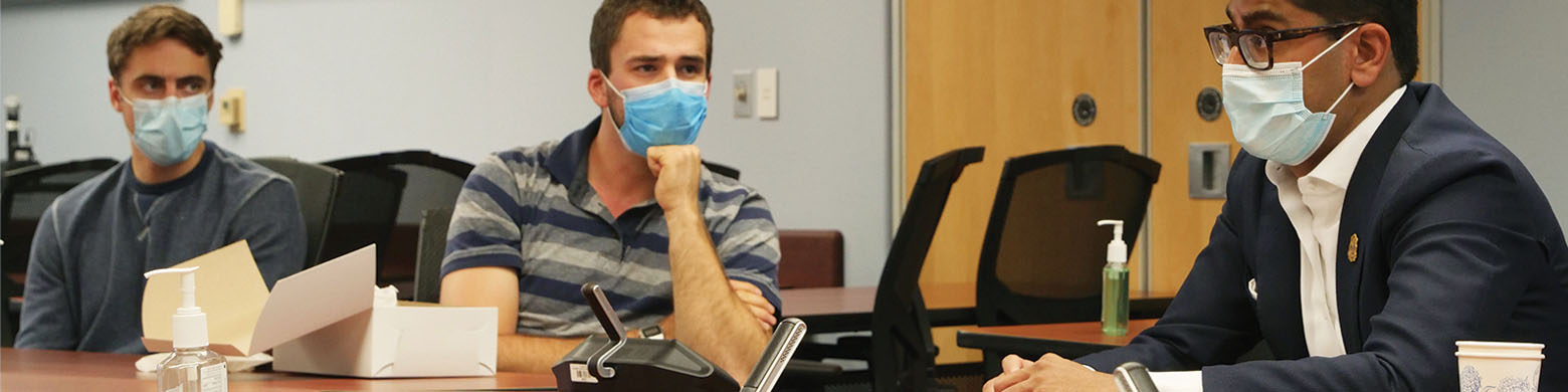 OMA president Dr. Adam Kassam sits at a boardroom table with two other men, wearing masks
