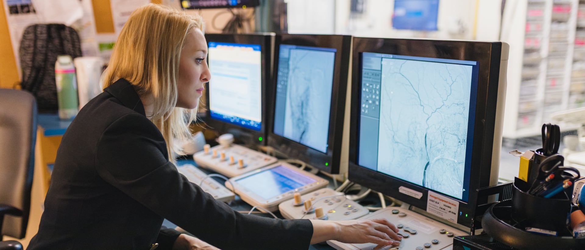 Dr. Luciana Catanese looking closely at brain angiograms on multiple computer monitors in a clinic settings.