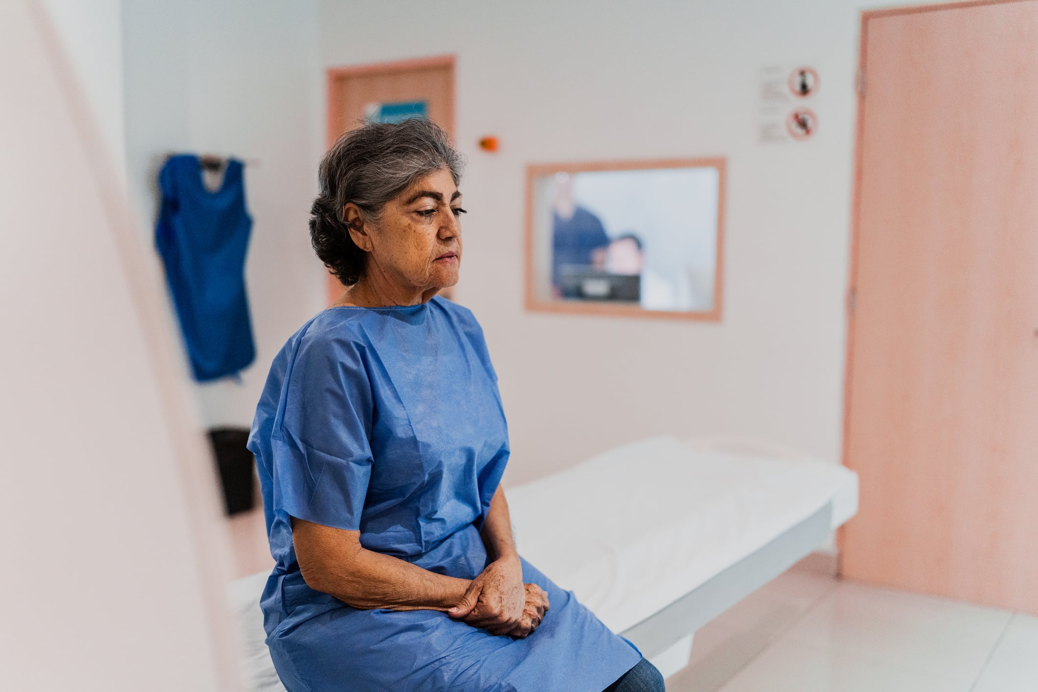 Patient wearing a blue hospital gown waits to be seen in a physician's office.