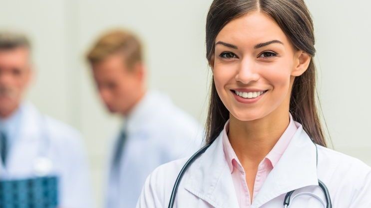 A female physician smiles at the camera with three other medical professionals in the background.