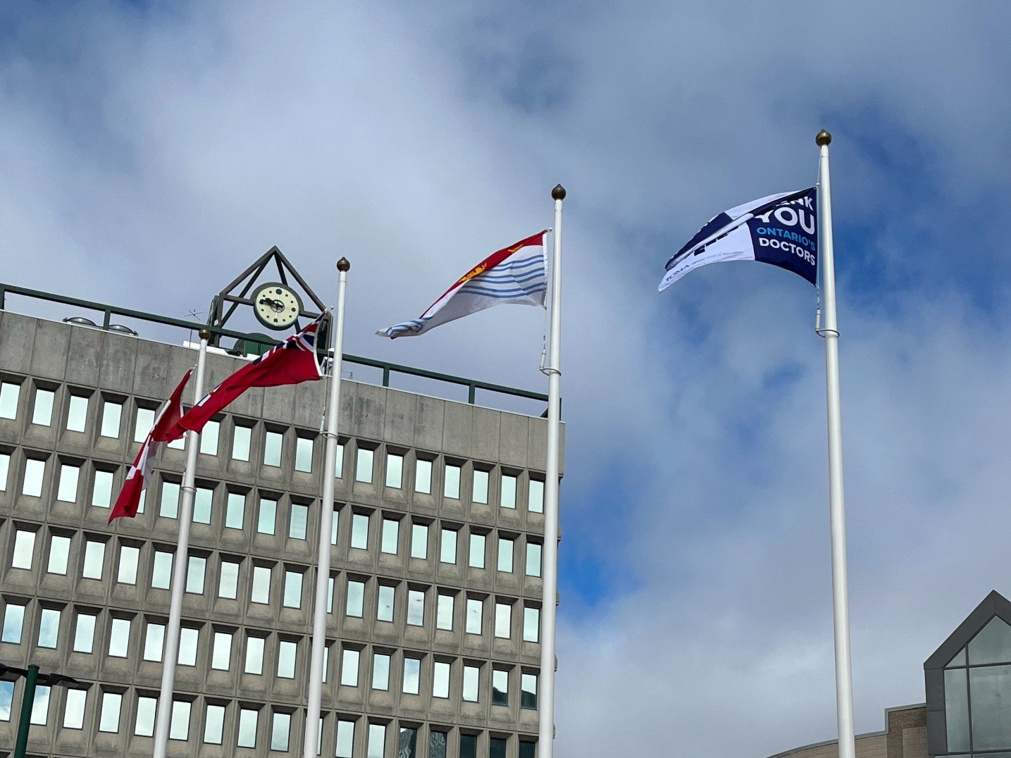 Three flags, including one that reads Thank You Ontario's Doctors, flutter in the breeze in London, Ont.