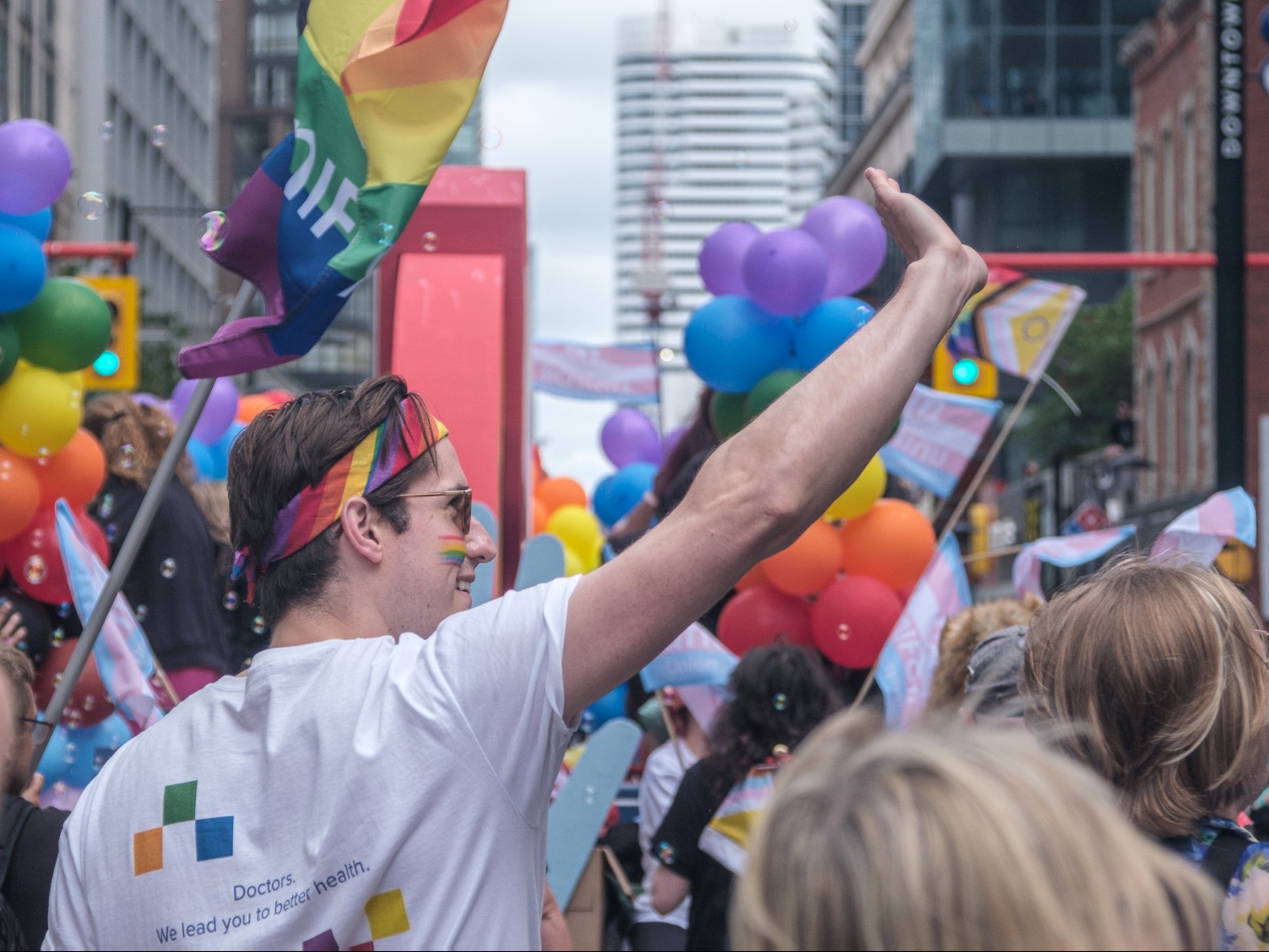 Dr. Nowak is seen from behind waving and smiling to a crowd, wearing an OMA Pride t-shirt and a rainbow bandana.