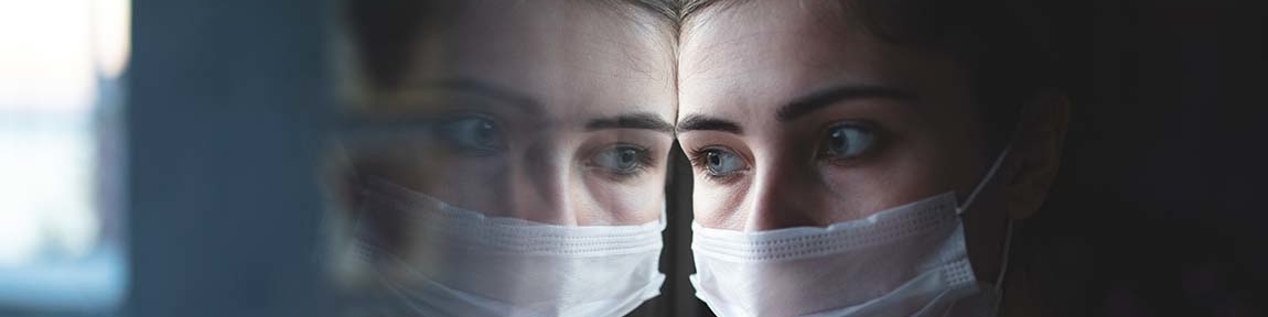 A woman wearing a surgical mask looking through a window.
