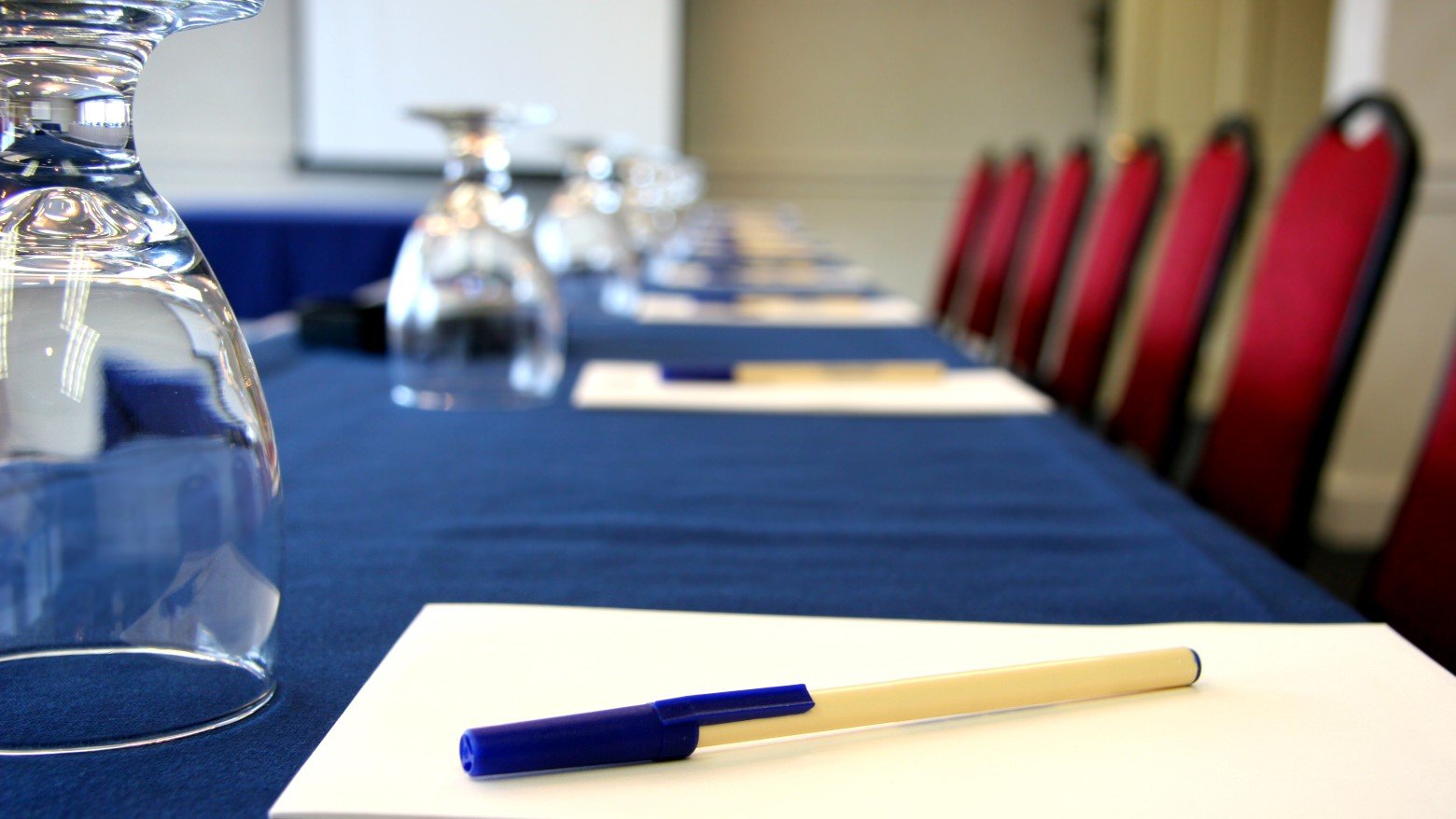 A conference table set with glasses, notepads, and pens, lined with red chairs in a professional meeting room.