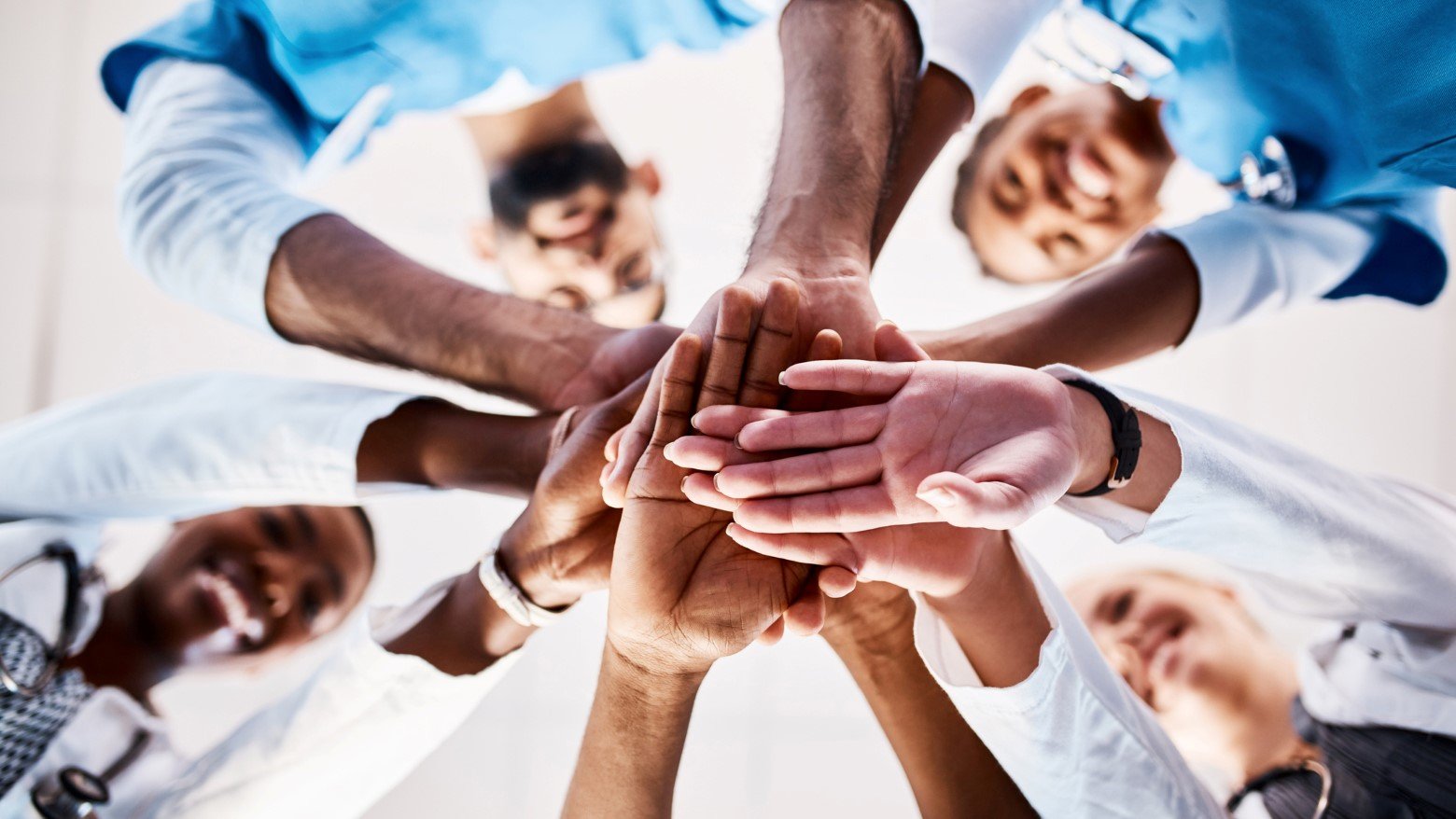 A diverse group of hands come together in a team gesture, symbolizing unity and collaboration in a professional setting.