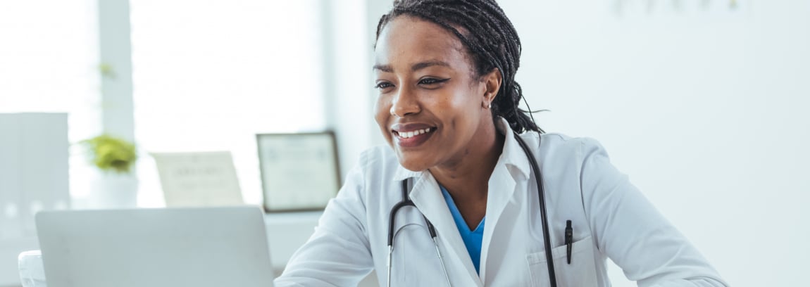 A physician looks at her laptop screen and smiles.