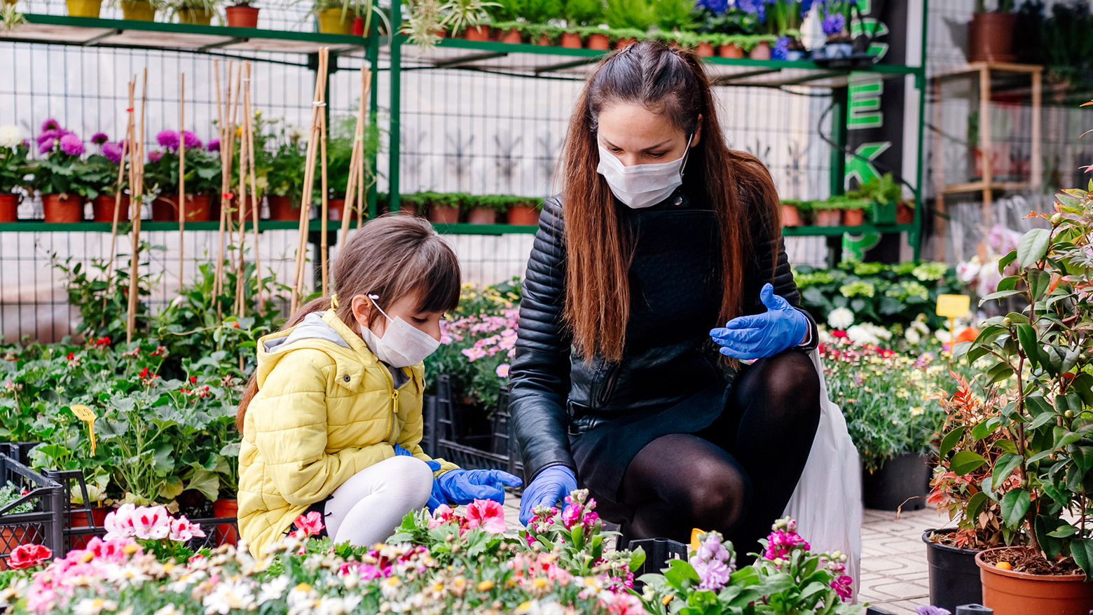 A woman and child in a garden centre crouched down looking at flowers.