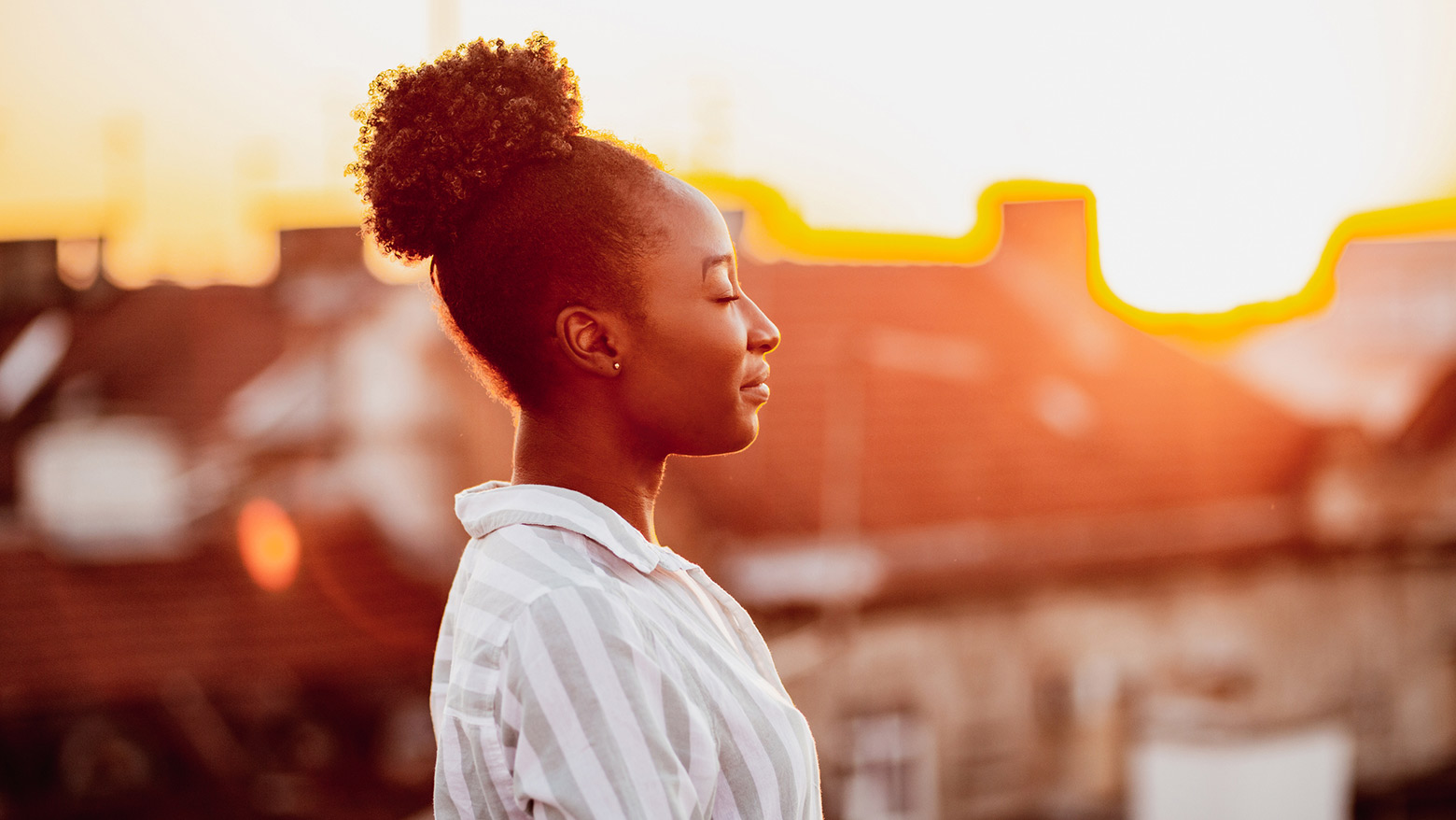 A woman standing with her eyes closed with the sun reflecting off her face.