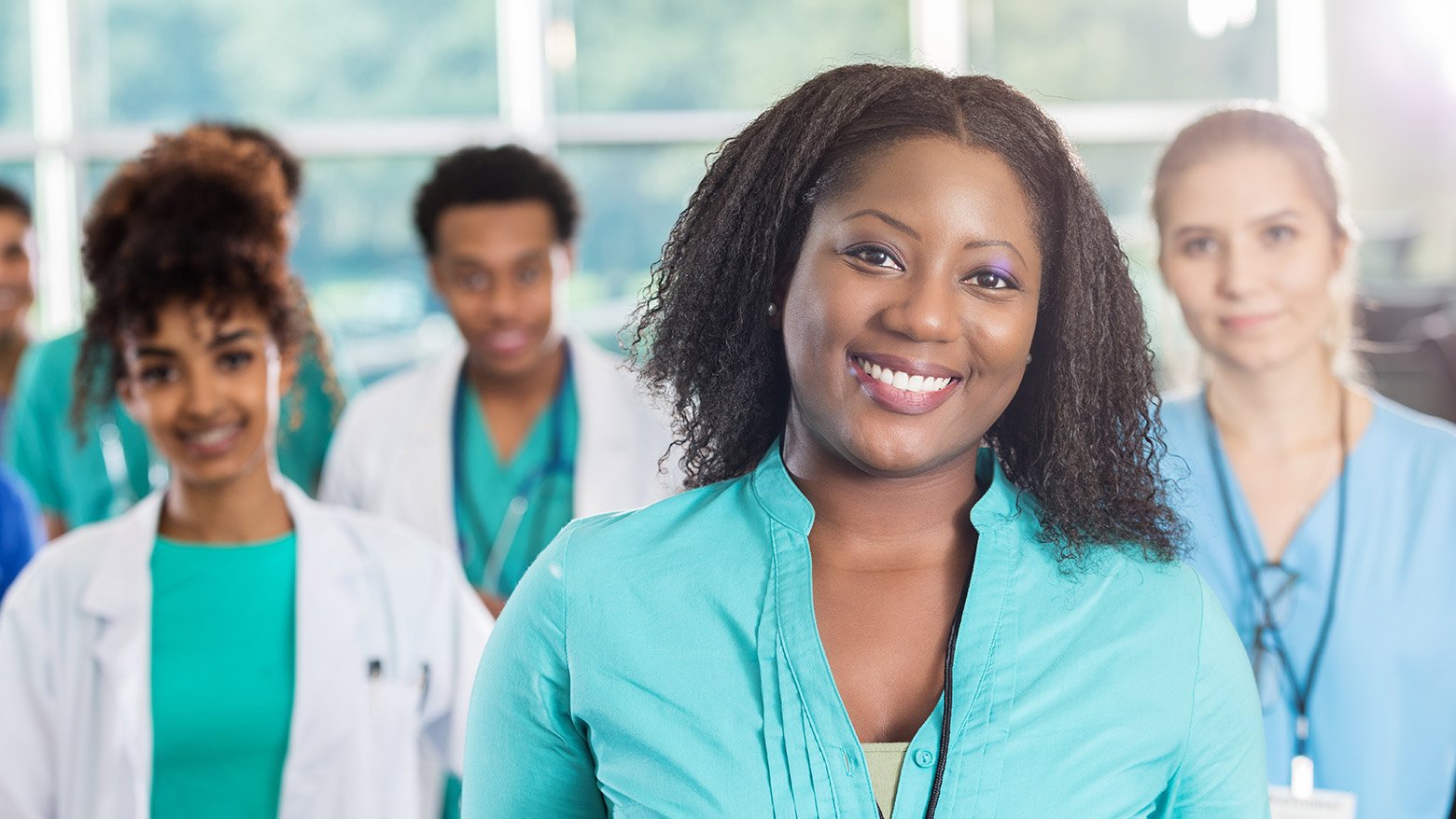 A woman smiling at the camera with co-workers standing behind her in scrubs.